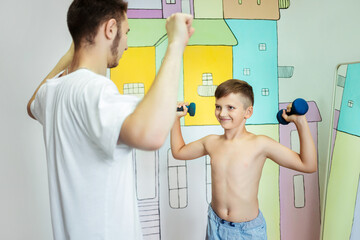 boy trains with a physiotherapist with dumbbells in a rehabilitation center. Smiling child with...