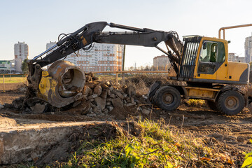 Photo of a yellow muddy excavator digging the ground at a construction site. Constructional concept