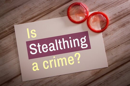 Conceptual keyword &ldquo;Is Stealthing a crime?&rdquo; printed on white card with two unused condoms on shabby chic wooden table. Stealthing is non-consensual condom removal during sexual intercourse