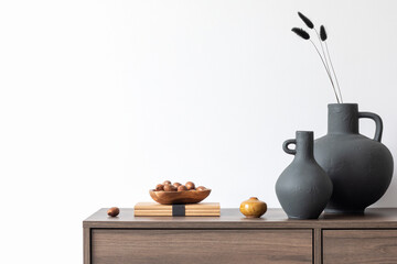 Creative minimalistic composition with white wall, vases and stylish personal accessories on wooden commode. Copy space. Template..