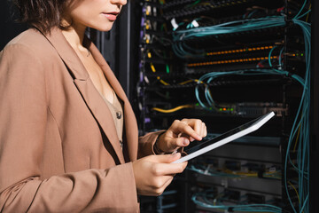 partial view of programmer using digital tablet while checking blurred server in data center