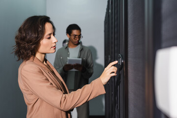 technician making diagnostics of server in data center near blurred african american colleague with digital tablet