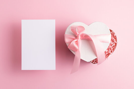 Blank card and festive gift box isolated on pastel pink background. Baby shower, Mothers day, Valentines day greeting mock-up.