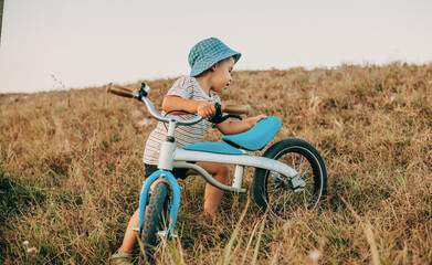 Fototapeta na wymiar Boy with blue hat and his bicycle on a grass field. Healthy lifestyle.