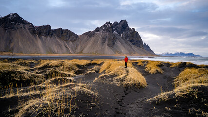 Woman in red jacket at Stokksnes, Iceland. Scenic image of tourist attraction. Travel destination. Discover the beauty of earth. Location Stokksnes cape, Vestrahorn (Batman Mount), Iceland, Europe.