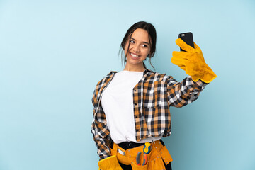 Young electrician woman isolated on blue background making a selfie