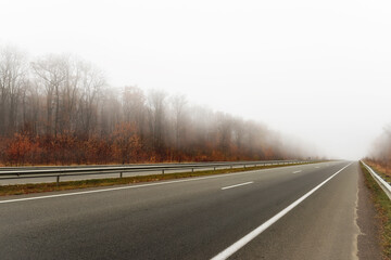 Asphalt deserted road in fog and autumn landscape along the road.
