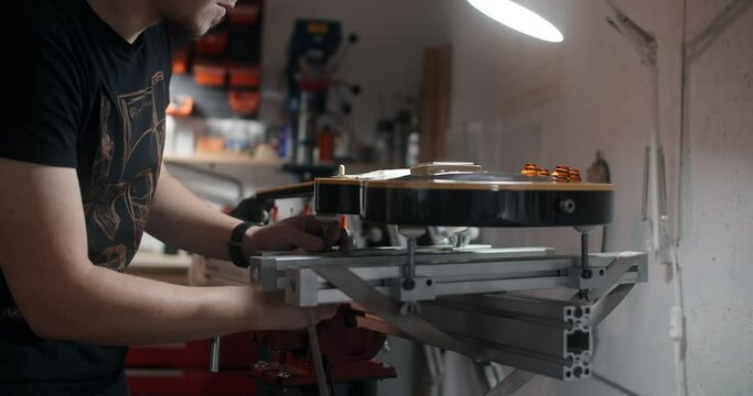 Guitar tech mounts the electric guitar on the jig at the musical instruments repairing shop, 4k 60p 10 bit
