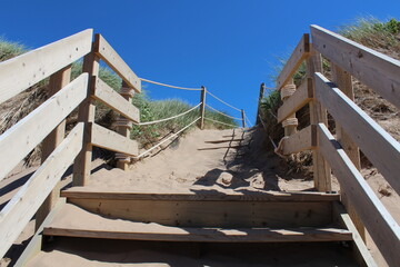 Tan coloured sandy path and wooden stairs with wooden railings against a clear blue sky with no...