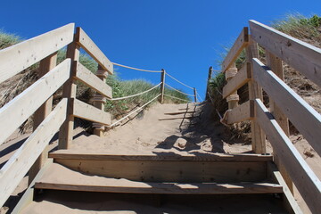 Tan coloured sandy path and wooden stairs with wooden railings against a clear blue sky with no clouds at PEI National Park (Maritimes, Canada)