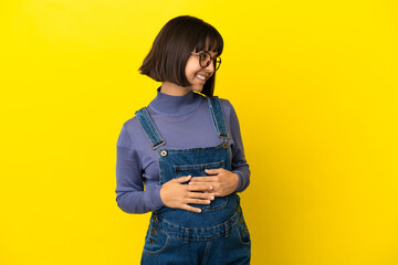 Young pregnant woman over isolated yellow background with arms crossed and happy