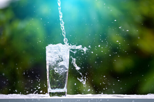 Drink water pouring in to glass over sunlight and natural green background.Water splash  in glass. glass of water in green garden blurred background.