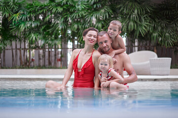 Fototapeta na wymiar Vacation with a family. Happy young parents and their kids having fun in swimming pool.