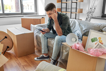 moving, eviction and real estate concept - sad man with smartphone and boxes at new home