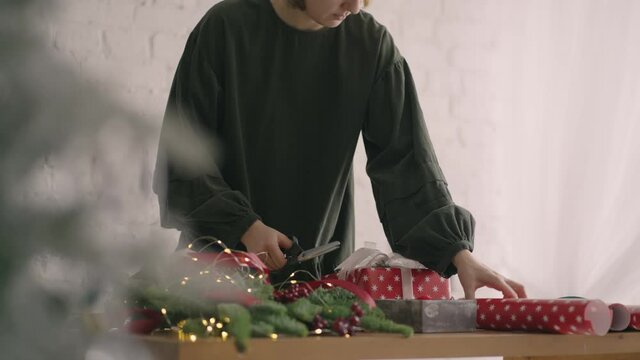 Crop hands decorating wrapped box with string. Female packing cardboard gift box various decorative items prepared for Christmas celebration. Detail female hands tying rope