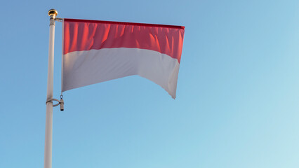 National flag of Monaco on a flagpole in front of blue sky with sun rays and lens flare. Diplomacy concept.