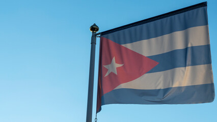 National flag of Cuba on a flagpole in front of blue sky with sun rays and lens flare. Diplomacy concept.