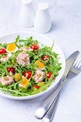Salad with tuna, arugula, tomatoes, olives and eggs in a white plate. A traditional dish. Close-up.