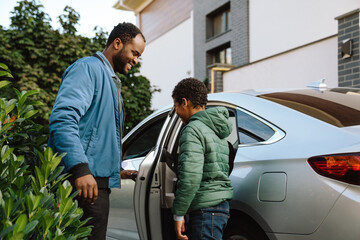 Black man an his son smiling and talking together while standing by car