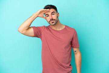 Fototapeta premium Young caucasian man isolated on blue background looking far away with hand to look something