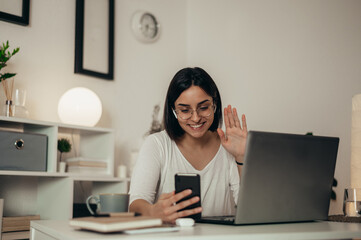 Woman using smartphone and a laptop for an online meeting while working from home