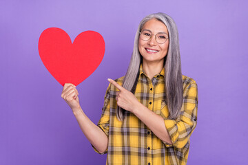 Photo of senior lady indicate finger heart shape ad choice suggest promo isolated over purple color background