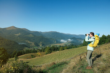 Fototapeta na wymiar Tourist with hiking equipment looking through binoculars in mountains
