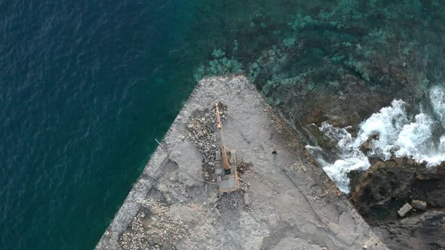 Aerial top down view isolated excavator at work. Excavator drilling a pier surrounded by blue sea ocean water. Strengthening shore coastline breakwater. Real estate construction on island