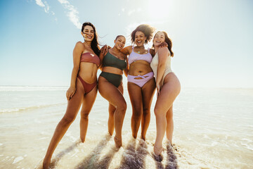 Happy female friends standing on beach water - Powered by Adobe
