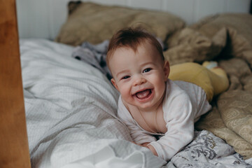 a happy baby in a white bodysuit is lying on the bed