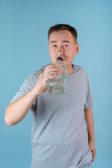 A drunk man drinks alcohol from a bottle standing on a blue background. Alcoholism and midlife crisis in men