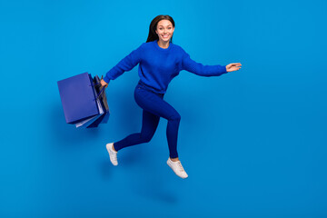 Full length body size view of attractive cheerful girl jumping carrying bags store outlet isolated on bright blue color background