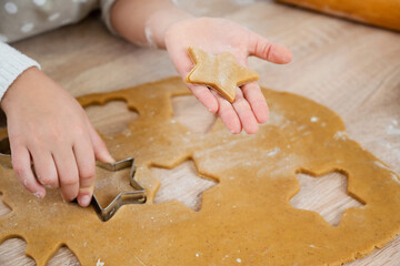 Child's hands cut cookies from dough with shape cutter