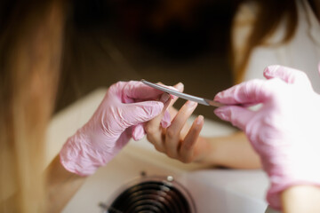Beauty saloon. Cute Caucasian girl young woman in pink gloves makes manicure client with long hair....