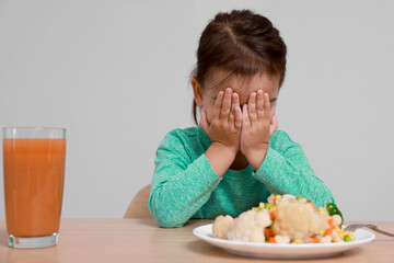 Cute little girl crying and refusing to eat vegetable salad at table on grey background