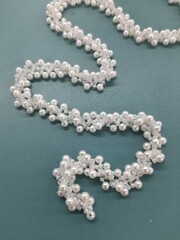 A braided beaded belt with white pearls is laid out randomly on a blue background.
