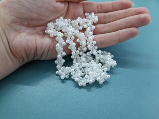 Wicker belt made of white pearls. The belt falls from his hand on the turquoise surface.