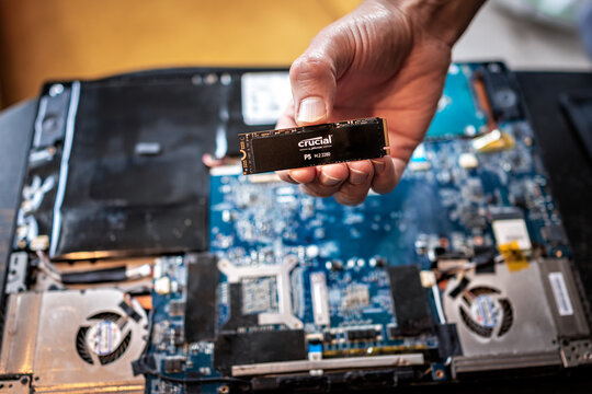 Banner Elk, USA - June 23, 2021: Macro closeup of hand holding Crucial micro chip by Micron and laptop computer keyboard for replacing dead hard drive