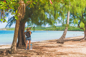 Woman with straw hat and striped bag on tropical beach near tree