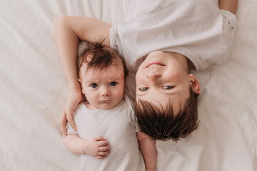 the brothers are lying on a white bed , hugging