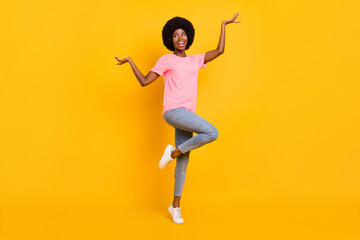 Full size photo of cool young lady look empty space dance wear pink t-shirt jeans isolated on yellow color background