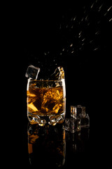 a glass of whiskey with ice and splashes on a black background
