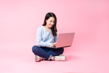 portrait of young asian girl sitting using laptop, isolated on pink background