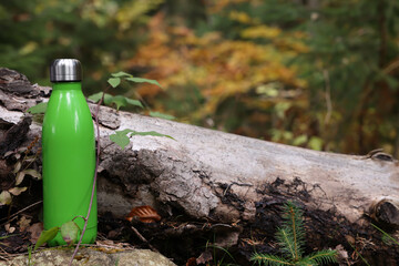 Green thermo bottle near log in forest