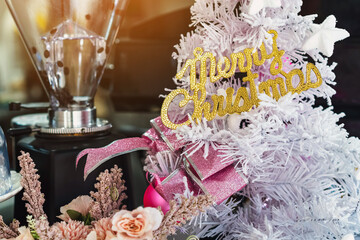 Golden shiny Merry Christmas handwriting logo on white paper tree for christmas time in coffee shop. Christmas tree decorations with color lights and a merry christmas logo in cafe. Selective focus