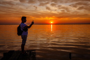 a man takes a photo on the phone of a pink salt lake at sunset. Ukraine