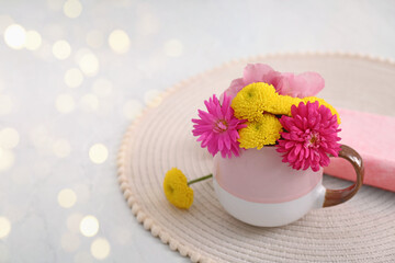 Beautiful bright flowers in cup on table, space for text