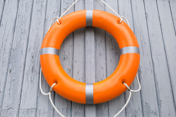 Orange life buoy hanging on light wooden wall