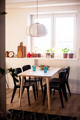 Cozy kitchen on a sunny day. Home atmosphere, light interior with black chairs. Flowers in pots on the window