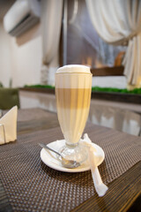 Coffee Latte Macchiato Layered Coffee in a see Through Glass Irish Coffee Glass. Cup is on a Wooden Table on windows